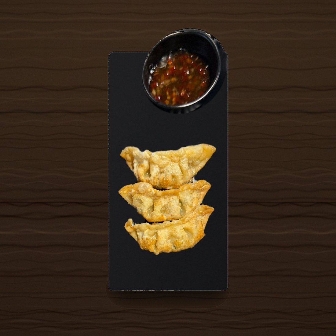 Trois gyozas aux légumes et leur sauce sur une assiette noire